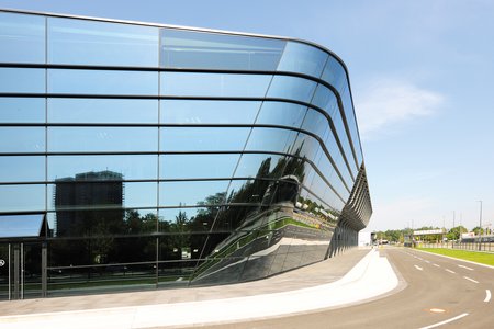 [Translate to Französisch:] Das trapezförmige Gebäude mit rund 9.600 m² Bruttoausstellungsfläche besticht durch seine gläserne Fassade, die einen offenen, lichtdurchfluteten Treffpunkt für Besucher, Aussteller und Veranstalter schafft.