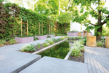 The linear composition of the themed garden follows the small ‘river’ with its little waterfall, paths, terraces and beds, bordered by violet raised beds in varying heights.