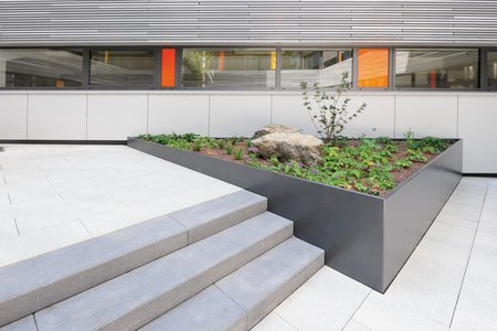 A set of three steps are harmoniously framed by the raised beds. Finished with a plastic coating in DB 703 iron mica, the beds create an appealing contrast with the light floor slabs in the courtyard. 