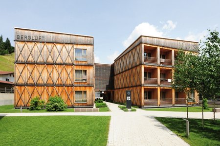 In den Sommermonaten fügt sich der Hotelbau dank der Holzkonstruktion ansprechend in das satte Grün der umliegenden Landschaft ein. Die warmen Töne der Fassade unterstreichen den einladenden Charakter des Komplexes.