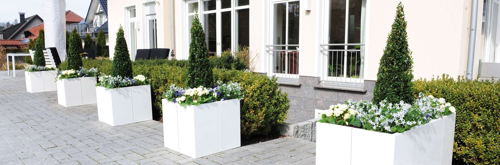 Modulare Pflanzkästen in weiß vor einem Haus mit blühenden Pflanzen
