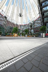  Ook de donkere bestrating blijft conform het motto “Bestaande constructies verstevigen door recombinatie“ gehandhaafd, maar de oude roestvrijstalen platen zijn nu vervangen door lichte granieten platen. De nieuwe gootdragers, waarvan de sleufperforaties gebaseerd zijn op het patroon van de vorige metalen afdekking, leiden het regenwater naar een eronder gelegen holle ruimte van 5 cm diep die uitmondt in de riolering.  Foto: Richard Brink GmbH & Co. KG