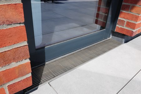 Cette embrasure a également été équipée d’un caniveau de drainage « Stabile ». La grille à tiges longitudinales crée ici un contraste habile avec la façade en briques. Elle s’intègre parfaitement dans le mélange de matériaux choisi pour ce bâtiment.  Photo : Richard Brink GmbH & Co. KG