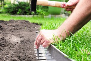 Die flexible Rasenkante von Richard Brink beim Einbau in einem Garten zwischen Beet mit Erde und grünem Rasen. Die Beeteinfassung wird am Auflageschenkel mit Erdnägeln befestigt.