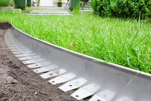 Die Rasenkante aus Metall mit Bördelung wird dauerhaft mit Erdankern fixiert