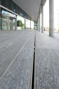 Stainless steel Lamina slotted channels by Richard Brink GmbH & Co. KG subtly integrate into the natural stone floor. They trace the entire base of the entrance area.