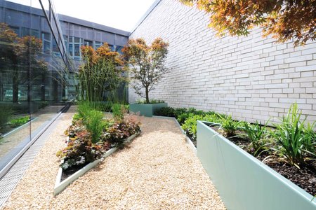 Op de kleinste van de twee binnenplaatsen overheersen de hoekige bouwstijlen en de rode tinten van de beplanting.