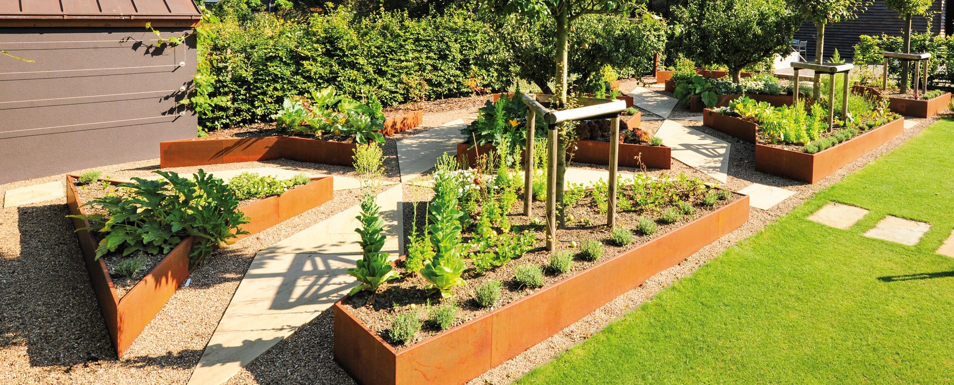 Individuell gefertigte Hochbeete aus Cortenstahl von Richard Brink nach Maß gefertigt mit grünen Pflanzen in einem ordentlichen Garten.