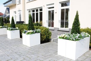 Modulare Pflanzkästen in weiß vor einem Haus mit blühenden Pflanzen