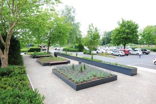 Pflanzbeete aus Aluminium mit grauer Lackierung von Richard Brink vor einem öffentlichen Gebäude mit grünen Pflanzen und Sitzbänken für eine schöne Umgebung